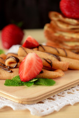 Golden crepes on a wooden board surrounded by fresh strawberries
