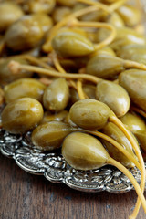 Pickled caper berries in metal dish .