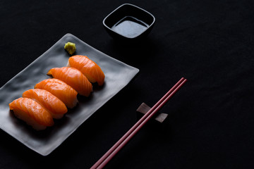Salmon sushi with green wasabi on Black plate or dish and shoyu sauce on black background