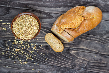 Rye bread on a wooden background near a bowl of wheat close-up.