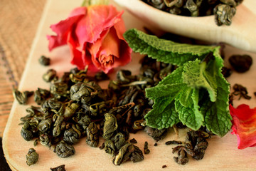 Leaf tea, dried rose and fresh mint for making a hot drink on a wooden board