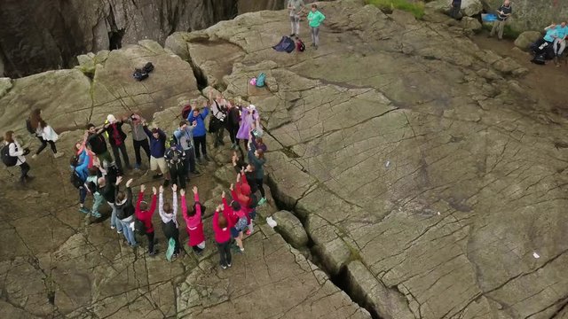 Aerial view from drone on breathtaking cliff called Preikestolen. Group of young people is standing on the cliff and making the heart and raising hands up with hands. 4k footage, upper view. Norway.