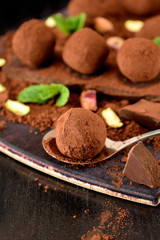 Chocolate truffles covered with cacao powder, pistachio nuts, chocolate and mint on a dark wooden board