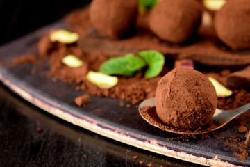 Chocolate truffles covered with cacao powder, pistachio nuts, chocolate and mint on a dark wooden board