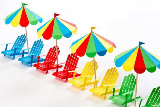 Bright umbrellas folding chairs are made of paper on a white background