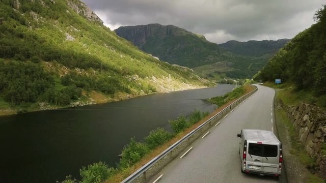 Aerial view on on the cars which are moving by breathtaking mountain road in Norway. Top view, green background full in trees and grass. 4k footage.