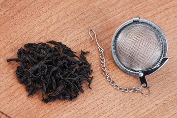 Black tea, and tea strainer with chain, on wooden background.