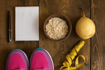 Bowl of oatmeal, Banana with yellow tape for measuring figure, empty notepad and trainers on dark...