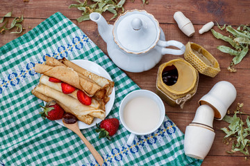 tea with milk, pancakes, honey and strawberries on a wooden brown table