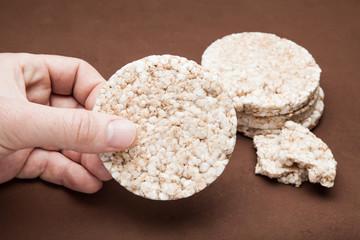 Hand hold rice bread on a brown background.