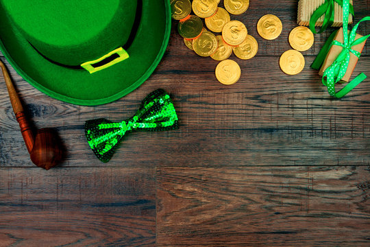 Saint Patrick's Day. Green hat of leprechaun, green bow tie, smoking pipe and gold coins on wooden background