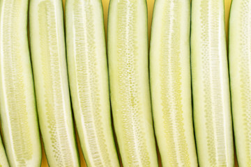 Cut lengthwise cucumbers laid out in a row on a yellow background