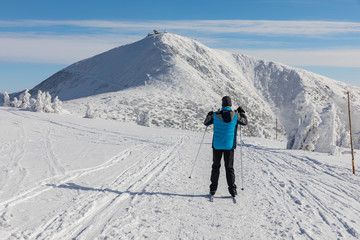 The man in a blue jacket goes on the cross country skiing in the Giant Mountains. In the background...