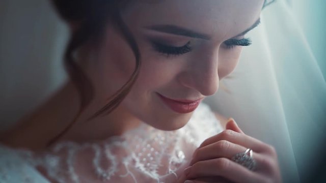 Close up view of attractive blue-eyed bride holding together her hands, dreaming, posing to camera, smiling happily. Sensuality, pureness, natural beauty. Moments of happiness