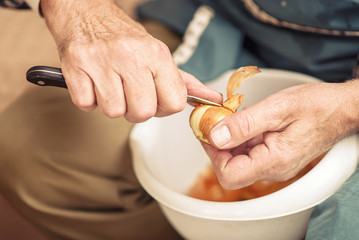 Senior elderly man peeling onion skin with a small sharp knife, preparing ingredients for lunch