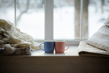 Fototapeta na wymiar Outside is cool.Two colored cup are on a window-sill express the warmness.