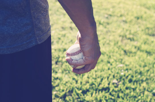 Sports image of baseball in the hand of pitcher.  Ball shows game equipment for the sport.