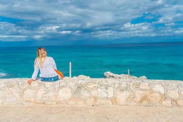 Beautiful outdoor view of woman sitting in a border enjoying the view of the beach of Isla Mujeres Punta sun caribbean sea, with a turquoise water and gorgeous sunny day in Mexico