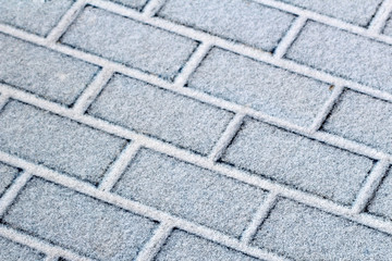Snow covered small paving tiles, the slabs after a snowfall. Winter pavement background.