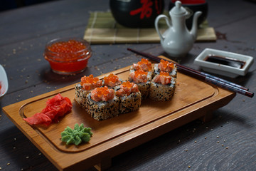 Sushi rolls served on a wooden plate in a restaurant. Sushi rolls and caviar on black wooden table. Japanese food.