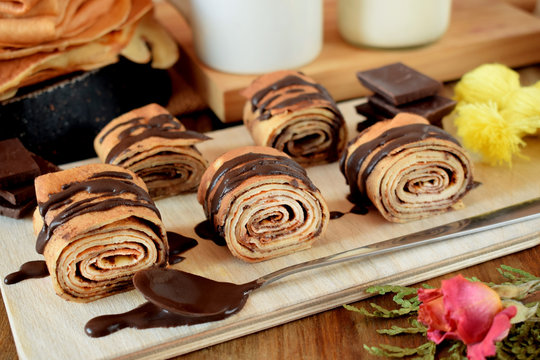 Crepes rolls with chocolate sauce on a wooden board