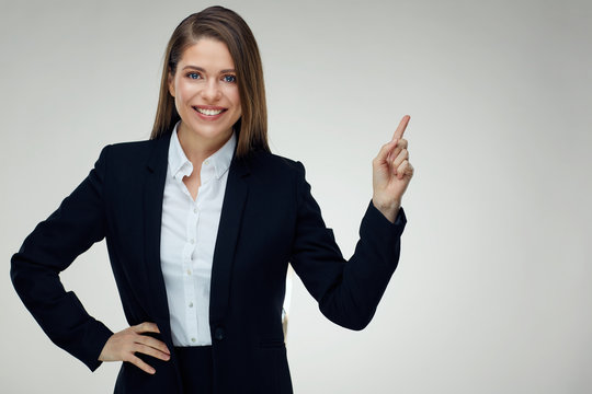 Smiling businesswoman wearing black suit pointing finger up at c