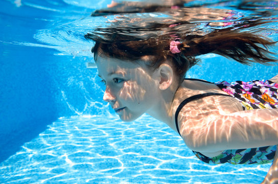 Child swims in swimming pool underwater, happy active girl dives and has fun under water, kid fitness and sport on family vacation on resort

