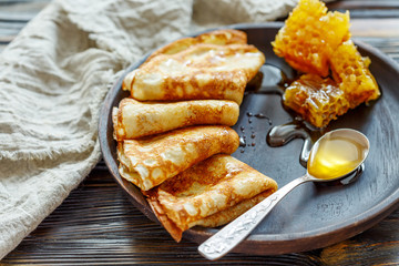 Crepes with honey on a wooden plate.