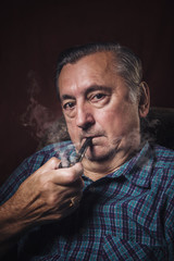 Classy senior elderly man smoking a pipe in his armchair, red background