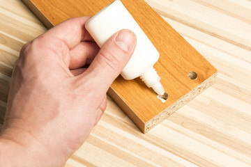 A hand applying glue to a wooden board. Sticking woodens pins. Home assembling furniture.