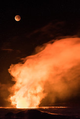 Moon eclipsing over volcano crater