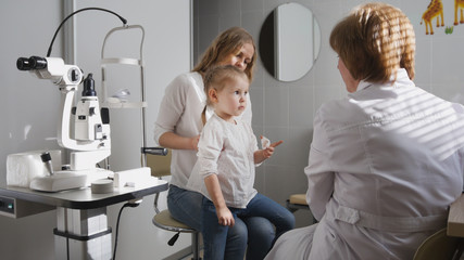 Ophthalmologist in clinic explains diagnosis about girl's eyesight - child plays