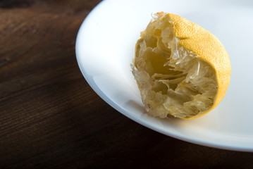 the squeezed-out lemon on a white plate on a wooden background