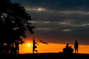 Silhouette of woman running with a kite beside her family