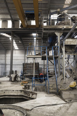Factory indoors. Giant industrial mixer acces stairs, crane with concrete deposit