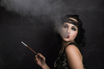 brunette girl in black dress in the style of decadence holds the mouthpiece and blows smoke