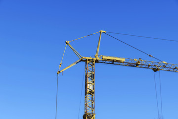 High construction crane of yellow color against the blue sky.