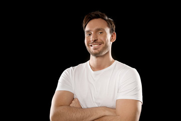 Handsome young man in a white t shirt isolated on a black background. Happy guy is smiling with his...