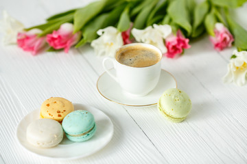 Coffee, pink and white tulips and macarons on the white wooden table