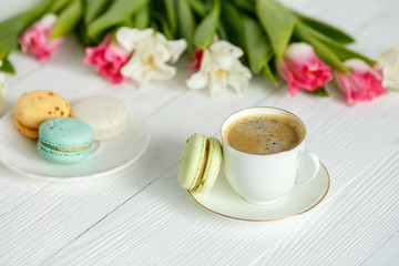 Coffee, pink and white tulips and macarons on the white wooden table