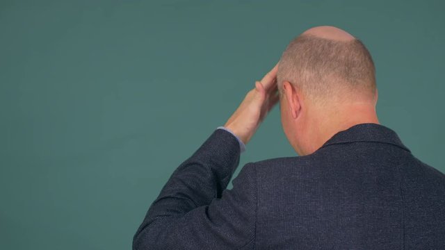 Mature bald man dressed in smart suit slaps his forehead