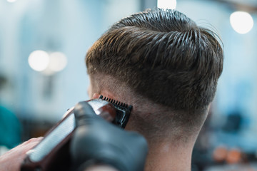 Getting perfect shape. Close-up side view of young bearded man getting beard haircut by hairdresser at barbershop. Soft focus.