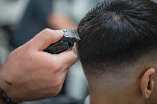 Man gets a cool haircut in barbershop. Barber makes the cut man electric razor. Men's care head. Soft focus.