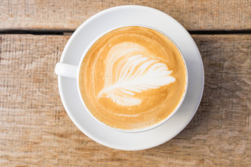 Close-up of a cup of coffee / cappuccino with foam and barista art on wooden table.
