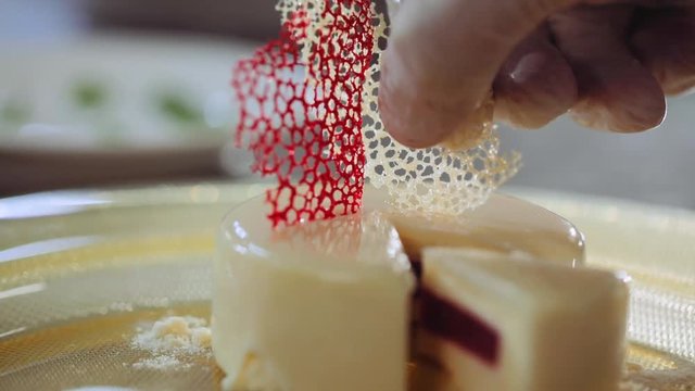 Confectioner&rsquo;s hand decorating a mini mousse pastry dessert covered with white chocolate with dark chocolate garnish decoration European cuisine restaurant, luxury Sweet tooth gourmet Vanilla dessert