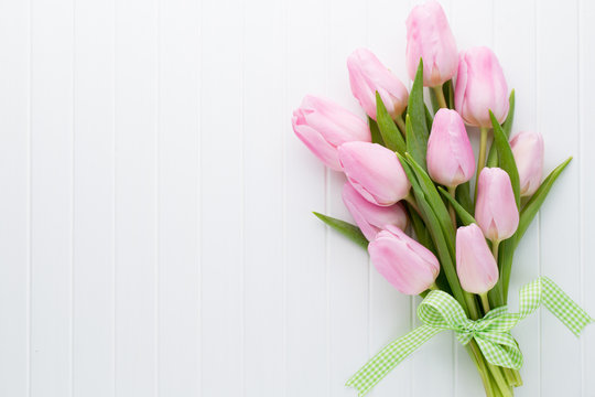 Fresh pink tulip flowers bouquet on shelf in front of wooden wall.