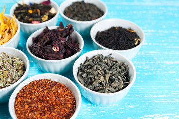 herbs and teas in bowls to make tea on blue table background cl