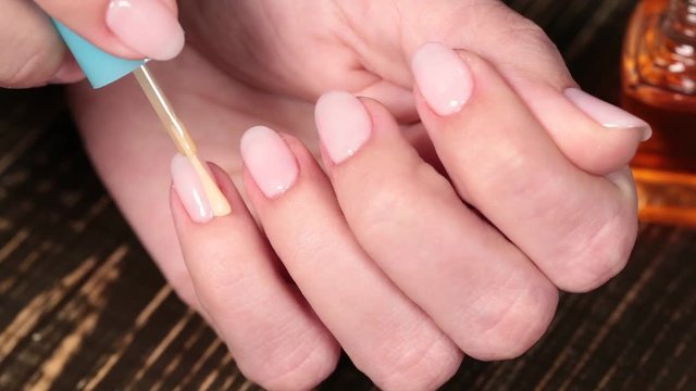 Closeup of female hands with beautiful natural fresh pink manicure. Woman applying oil to cuticles of fingers.