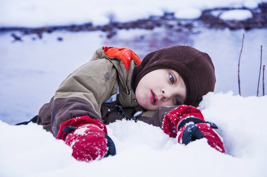 Tired child lies in the snow. A steep cliff of the river bank (сoncept dangerous winter game)