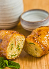 Close up, front view of a breakfast spring roll, cut in half with a sprig of mint and a glazed, pottery cup and bottle on a bamboo cutting board